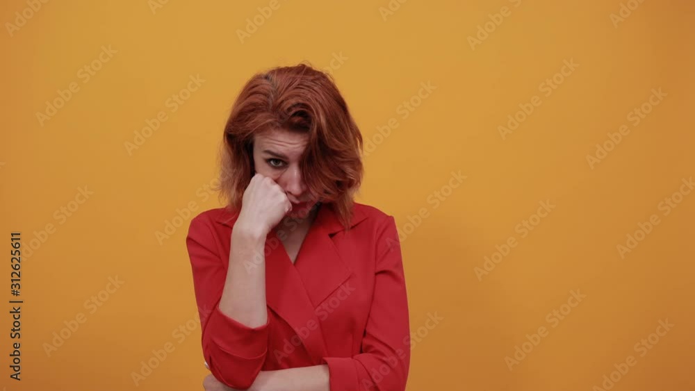 Boring caucasian woman looking at camera, pointing fist aon cheek, keeping hand on stomach wearing fashion red jacket over isolated orange background. People lifestyle concept. Boring caucasian woman looking at camera, pointing fist aon cheek, keeping hand on stomach wearing fashion red jacket over isolated orange background. People lifestyle concept.