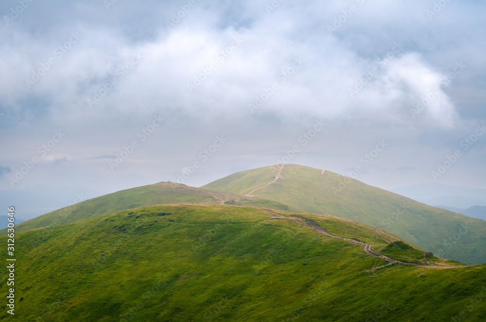 Fototapeta premium Beautiful mountain landscape with clouds. The road on the green top of Mount Ghimba in the Carpathians.