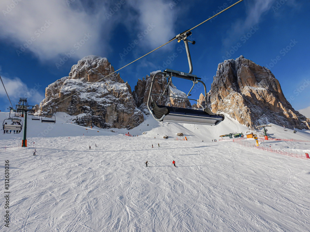Obraz premium Ski lift with chair and skiers in front of mountain with snow and blue sky
