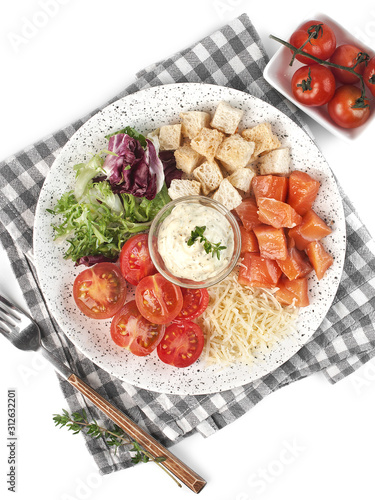 Caesar salad with red fish laid out according to the ingredients on a light plate on a white background isolated top view