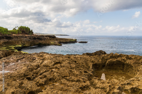 Rocky shoreline at Devil's Tear on island of Nusa Lembongan, Bali, Indonesia. Rocky shore with tidepool in foreground. Shoreline, ocean, sky & clouds in the background. 