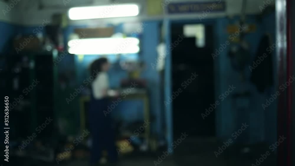 The concept of gender equality. A pretty young woman in a work uniform, working at the machine, the frame in a blur, and then comes and wipes her hands, face close-up. Work in an auto repair shop