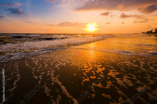Beautiful cloudscape over the sea with soft wave of blue ocean on sandy beach during sunrise.