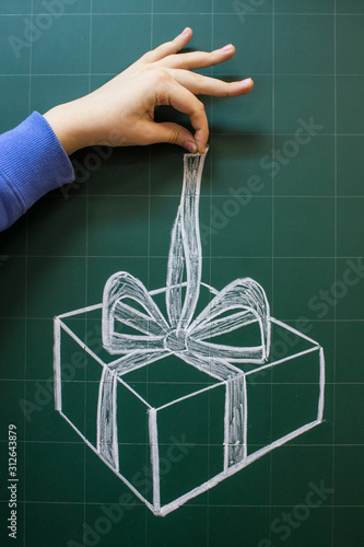 A gift box with a bow is drawn on a school green Board and the hand of a teenager gives it
