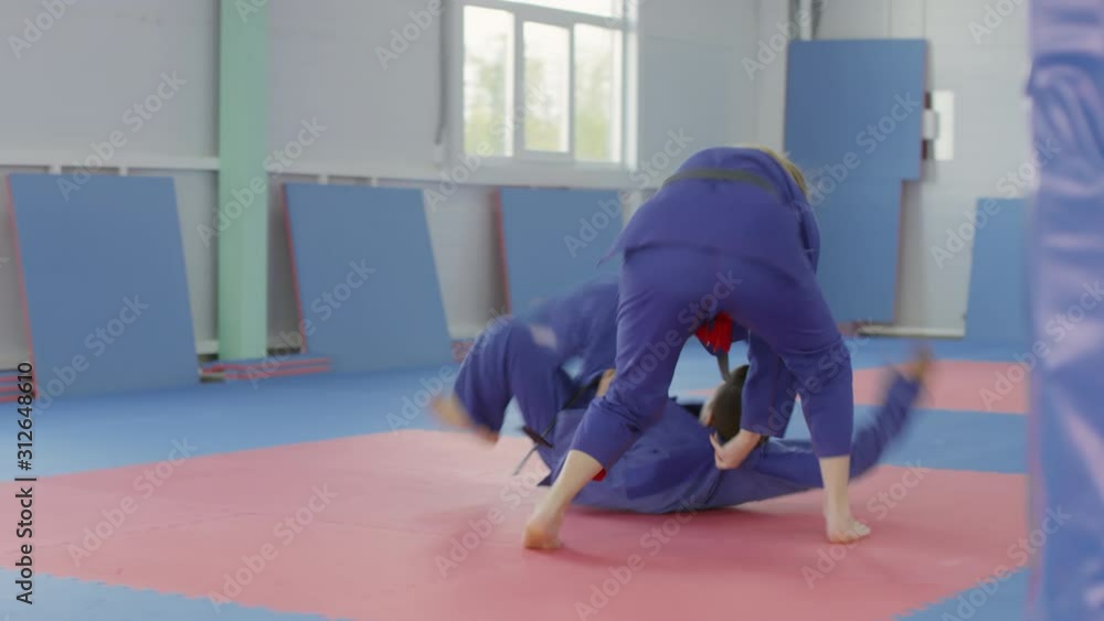 Female jiujitsu athlete kicking male opponent and throwing him on the