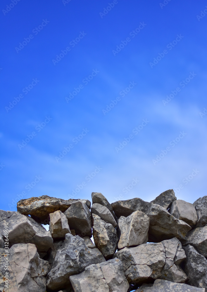 Stone Wall. Handmade, fence. Stone wall with a blue sky with clouds. With a lot of copy space. Vertical photo. Stone Wall. Handmade, fence. Stone wall with a blue sky with clouds. With a lot of copy space. Vertical photo.