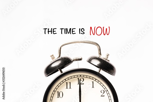 “THE TIME IS NOW” wordings with alarm clock against white background