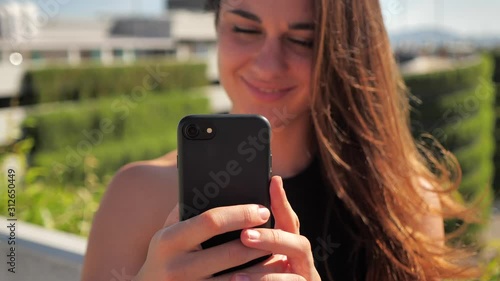 close-up portrait of smiling young elegant bissneswoman lwith deep brown eyes in black dress trying to buy something enjoyable with her smartphone Urban city background. Slow motion 4k photo