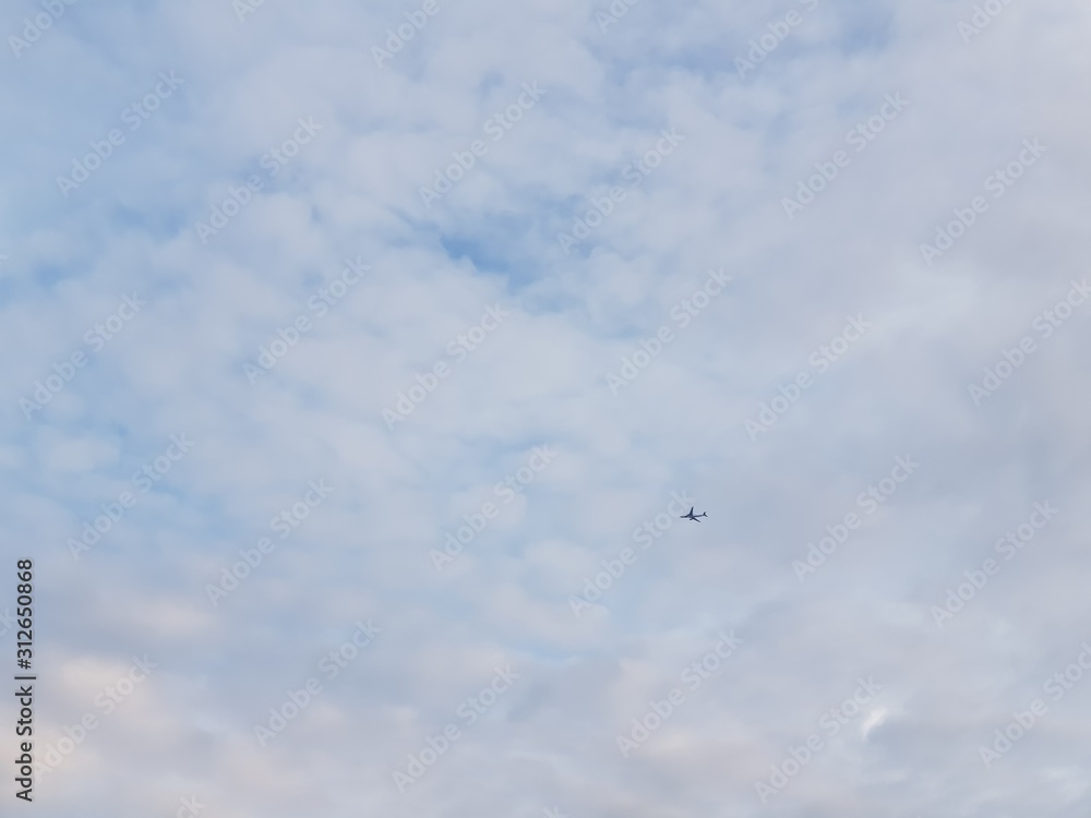 Tiny airplane on a vast cloudy sky