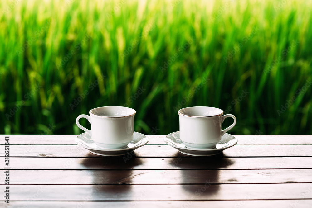 White tea cups on a beautiful background. White coffee cups against the background of rice terraces in Bali. Two white tea cups on saucers. Cups on a beautiful background. Still life White tea cups on a beautiful background. White coffee cups against the background of rice terraces in Bali. Two white tea cups on saucers. Cups on a beautiful background. Still life
