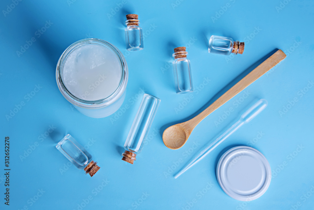 Coconut oil cosmetics for skin and hair care. Oil in small bottles, cream jar, bamboo spoon, dropper on light blue background. Top view. Flat lay. Coconut oil cosmetics for skin and hair care. Oil in small bottles, cream jar, bamboo spoon, dropper on light blue background. Top view. Flat lay.