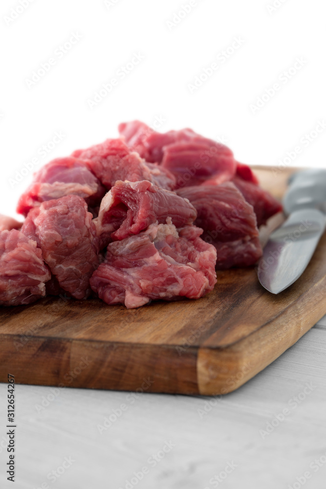 Beef brisket, diced cubed, on a wooden chopping board with a knife.  Grey wood background