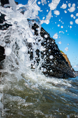 a sea wave is breaking on stones on a bright summer day. Close-up. Spray fly right into the frame.