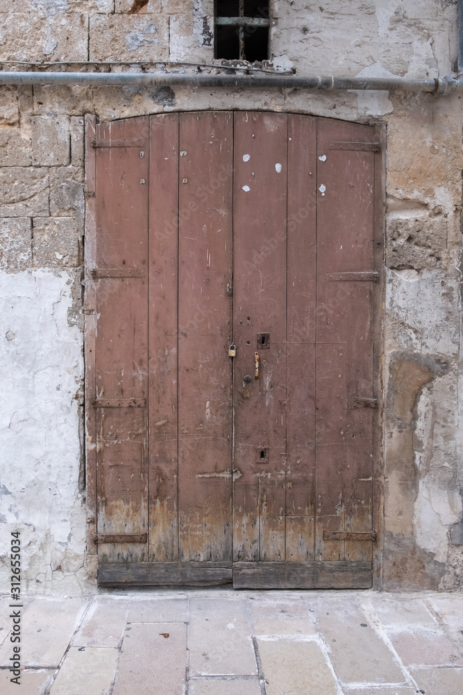 Old closed wooden door and padlock, closeup. Stone wall. Peeling paint.