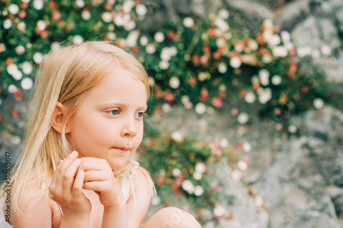 Outdoor summer portrait of adorable 5 year old little girl playing with daisy flowers