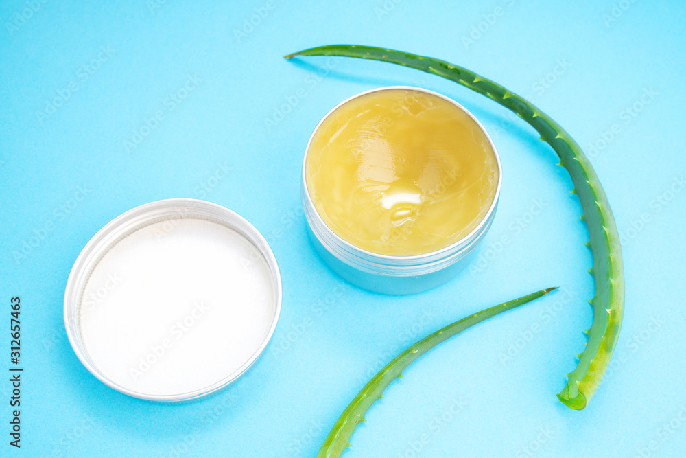 Top view of aloe vera leaf and container with organic moisturizing cosmetic cream on the blue background. Top view of aloe vera leaf and container with organic moisturizing cosmetic cream on the blue background.