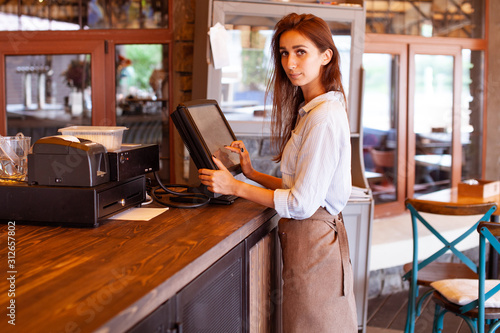 Close-up view of waitress registrated orders to the payment terminal. Young and beautiful waitress stand near sale terminal and check the order.