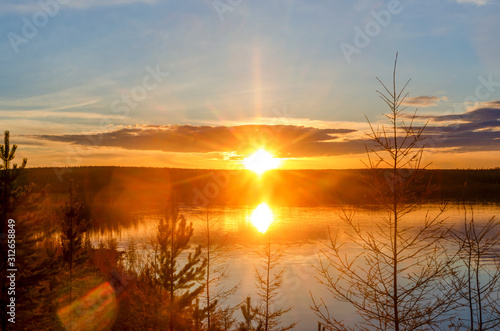 Bright colorful sunset with a sunbeam on the Vilyuy river in the Northern taiga of Yakutia Suntar against the background of fir trees on the shore under a cloudy sky.