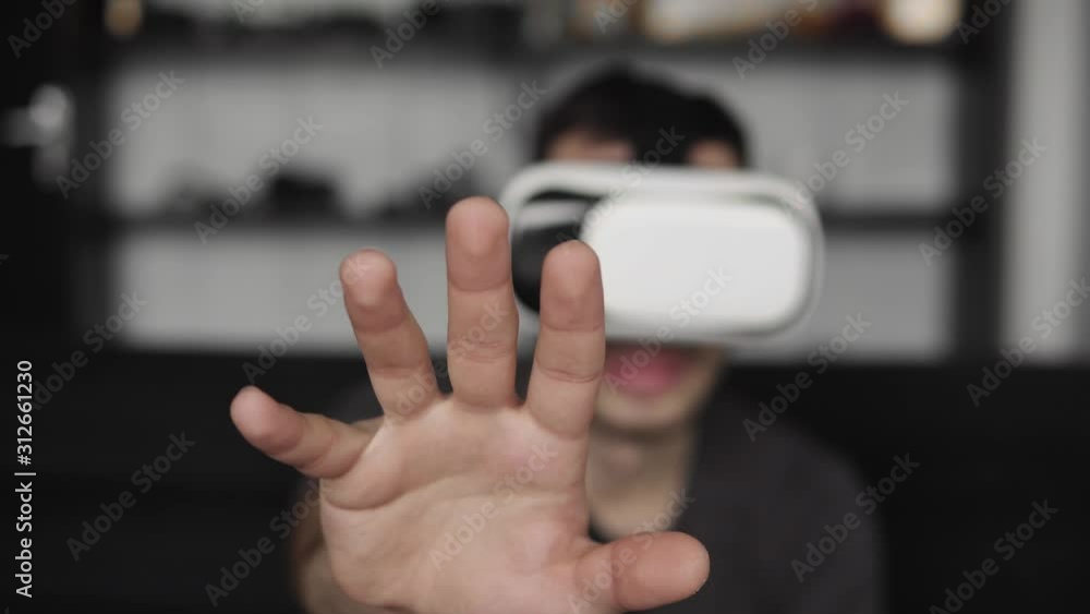 Young bearded man wearing headset of virtual reality in office sitting on a sofa and trying to touch something that he see in virtual world. Young bearded man wearing headset of virtual reality in office sitting on a sofa and trying to touch something that he see in virtual world.