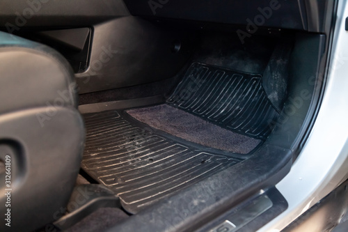 Dirty car floor mats of black rubber under passenger seat in the workshop for the detailing vehicle before dry cleaning. Auto service industry. Interior of sedan.