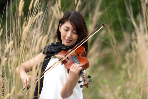 Beautiful asian woman hold violin,stand on grass background,in emotion feeling happy.