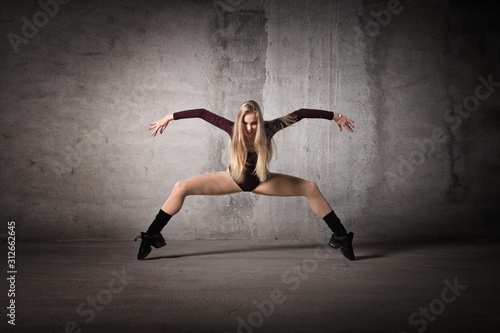 Fototapeta Naklejka Na Ścianę i Meble -  Blonde dancer stands on fingers on a gray background, dance pose, dance, body shape, fitness, training, strength