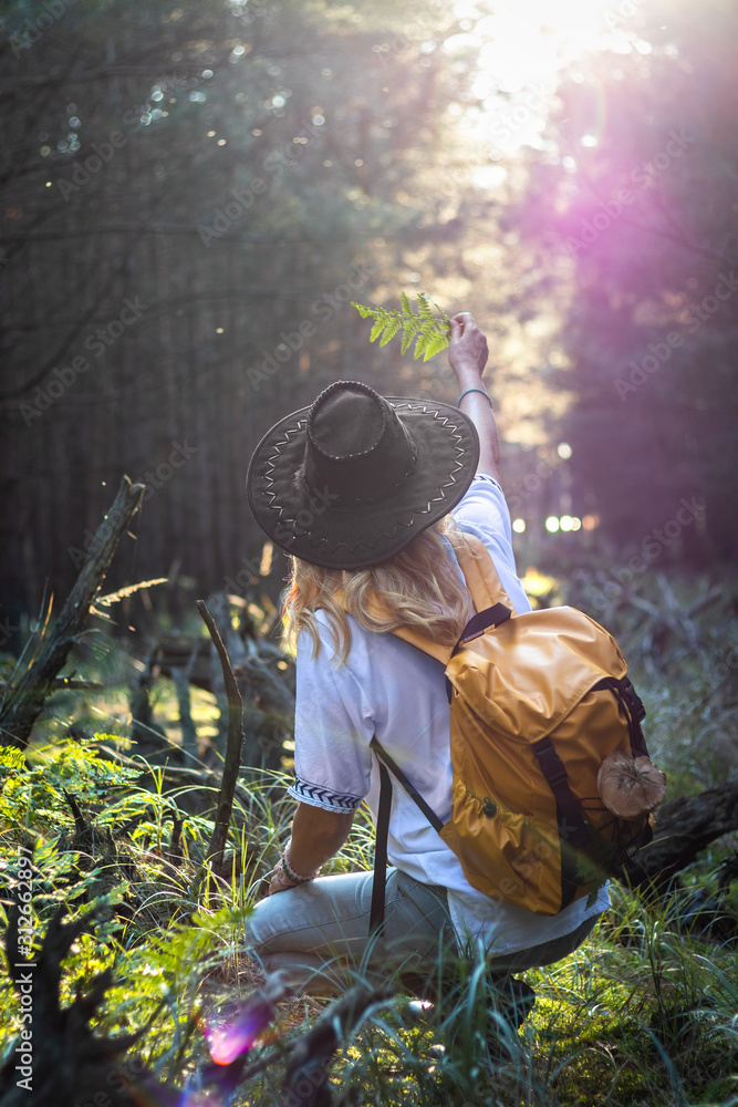 Hiking woman with hat and backpack looking into sun in forest