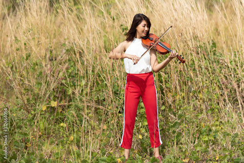 Beautiful asian woman hold violin,stand on grass background,in emotion feeling happy. photo