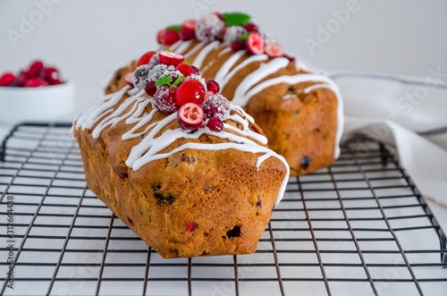 Traditional fruit cake with mixed fruit and cherries decorated with sugar icing, cranberries, pomergranate and cherry on a metal wire rack on a white background. Horizontal orientation. Close up. photo