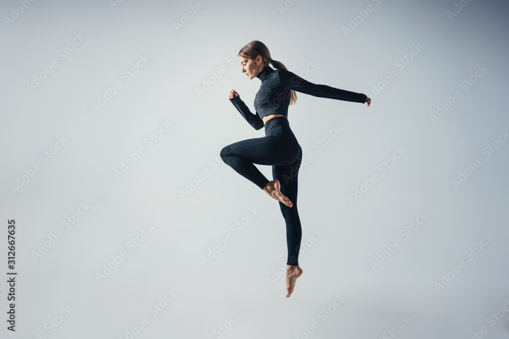 Fit sporty woman jumping and running in studio against white color background. Young handsome girl in jumping moment