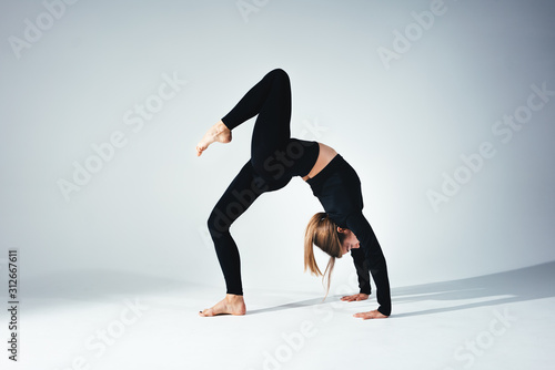 Young handsome fit woman wearing black sportswear doing stretching body against white background. Studio shot. Flexible girl doing yoga poses in white room