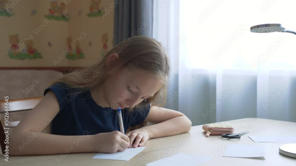 Teenager girl writing by pen on paper sheet at table on window background. School girl writing with pen on checkered paper on table desk in home office room Teenager girl writing by pen on paper sheet at table on window background. School girl writing with pen on checkered paper on table desk in home office room