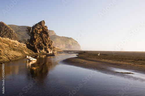Rock formations, black sand, river and mountains of Karekare Beach in West Auckland, New Zealand.