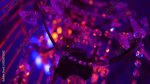 Old crystal chandelier with a metal frame in a night club in the spotlights light shimmers with blue and pink light giving glare