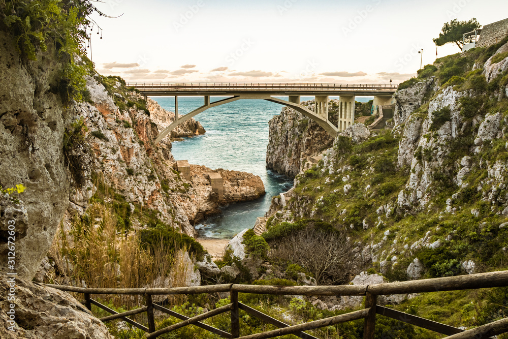 Fototapeta premium The Ciolo bridge, which connects two high cliffs, in an inlet of the sea, in Gagliano del Capo, near Santa Maria di Leuca, in Salento. In the evening, at sunset, in the winter. Puglia, Italy.