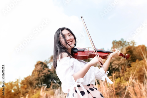 The abstract art design background of beautiful woman playing violin with smile and happy feeling ,enjoy with string instrument,in a park,vintage tone,blurry light around