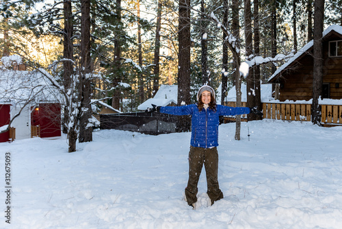 Local mountain community teenager girl has arms out to collect the falling snow in the snow covered yard of home. photo