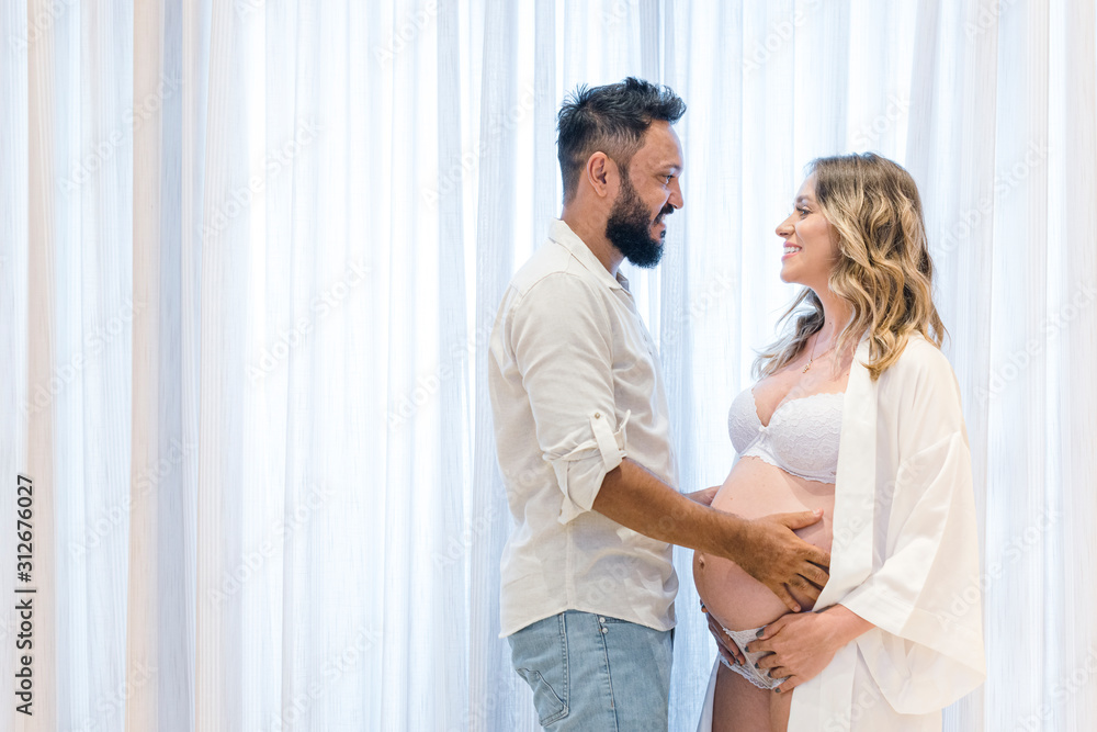 Handsome Latin man and his beautiful pregnant wife, couple looking at each other. Curtain background. pregnancy concept. Handsome Latin man and his beautiful pregnant wife, couple looking at each other. Curtain background. pregnancy concept.