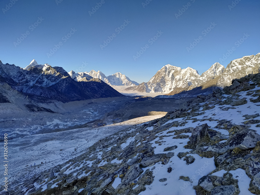 Taboche and Kangtega mountain peaks rises above Khumbu glacier and valley covered with clouds in the early morning in Himalayas. Theme of trekking in Nepal. Clear blue sky. Taboche and Kangtega mountain peaks rises above Khumbu glacier and valley covered with clouds in the early morning in Himalayas. Theme of trekking in Nepal. Clear blue sky.