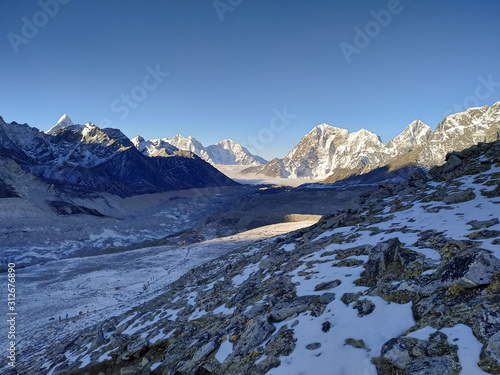 Taboche and Kangtega mountain peaks rises above Khumbu glacier and valley covered with clouds in the early morning in Himalayas. Theme of trekking in Nepal. Clear blue sky.