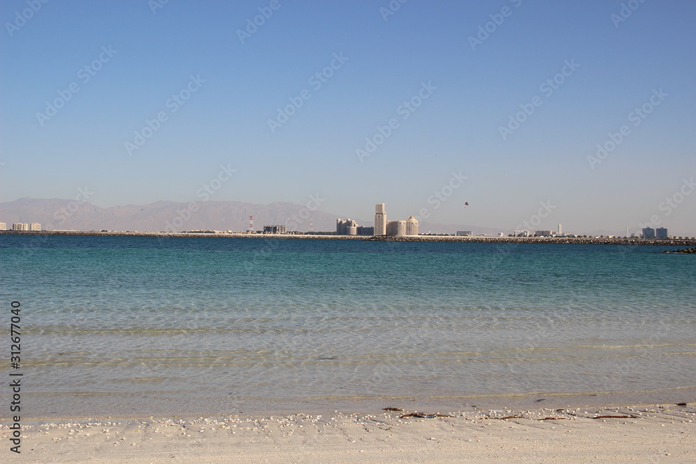 white sea coast sand in water with background of sea, buildings, mountains, blue sky