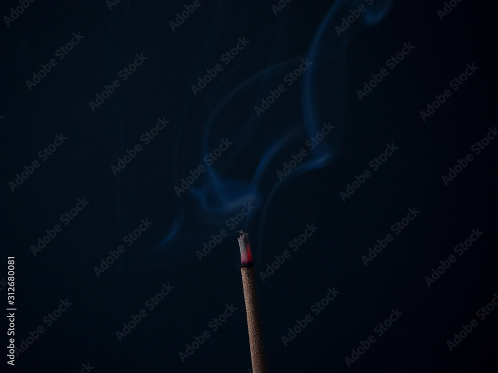 Aromatic incense stick is burning with beautiful gray curls of smoke on a black background in a meditation room. Used for aesthetic reasons, aromatherapy, meditation, and ceremony. Aromatic incense stick is burning with beautiful gray curls of smoke on a black background in a meditation room. Used for aesthetic reasons, aromatherapy, meditation, and ceremony.