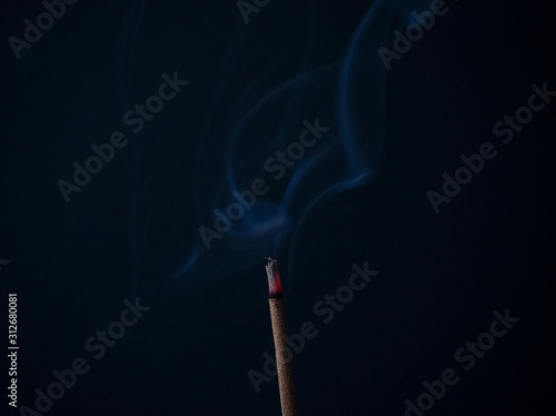 Aromatic incense stick is burning with beautiful gray curls of smoke on a black background in a meditation room. Used for aesthetic reasons, aromatherapy, meditation, and ceremony.
