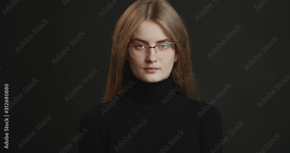 Attractive young woman in eyewear and black turtleneck sweater looking to camera isolated on dark background Attractive young woman in eyewear and black turtleneck sweater looking to camera isolated on dark background