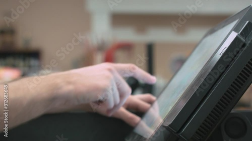 A profile shot of hands typing and making selections at a POS (Point Of Sale) system at a grocery store, shot under fluorescent lights. No distinguished branding.