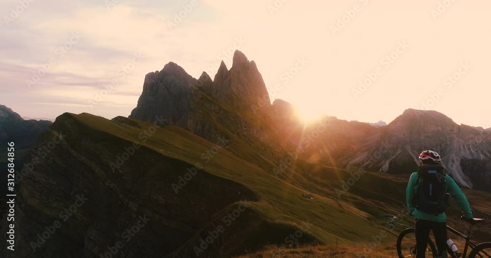 Aerial view. Young man with mountain bike arriving at Seceda mountain peak at sunrise. Puez Odle, Trentino, Dolomites, Italy. Aerial view. Young man with mountain bike arriving at Seceda mountain peak at sunrise. Puez Odle, Trentino, Dolomites, Italy.