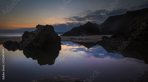 Rockpools and reflections at sunset on Three Cliffs bay on the Gower peninsula, Swansea, Wales, UK