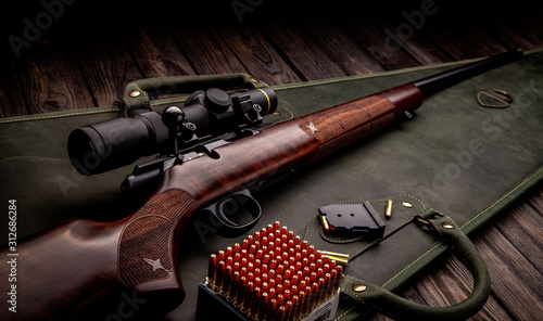 Classic bolt carbine .22lr with a wooden butt with a telescopic sight on a dark wooden background. Cartridges for a rifle next to a weapon. Hunter set.