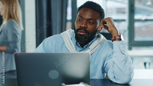 Sad tired african american business man touching head working hard on laptop upset exhausted young office work worried sleepy stressed frustrated employee corporate slow motion photo