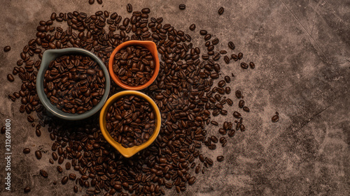 Fresh raw organic coffee beans in many colorful cups with varied sizes scattered on a slate countertop